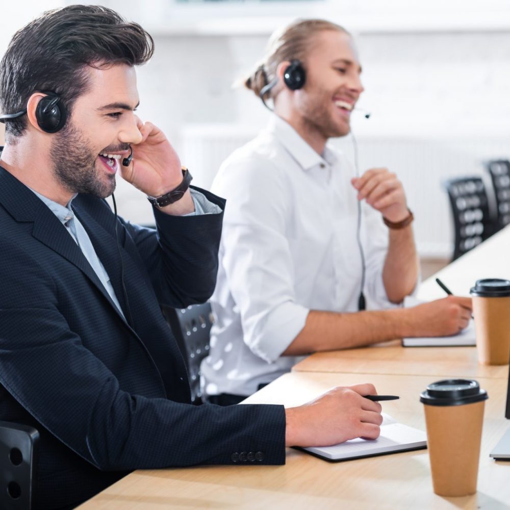 side view of male call center operators in headsets at workplace in office