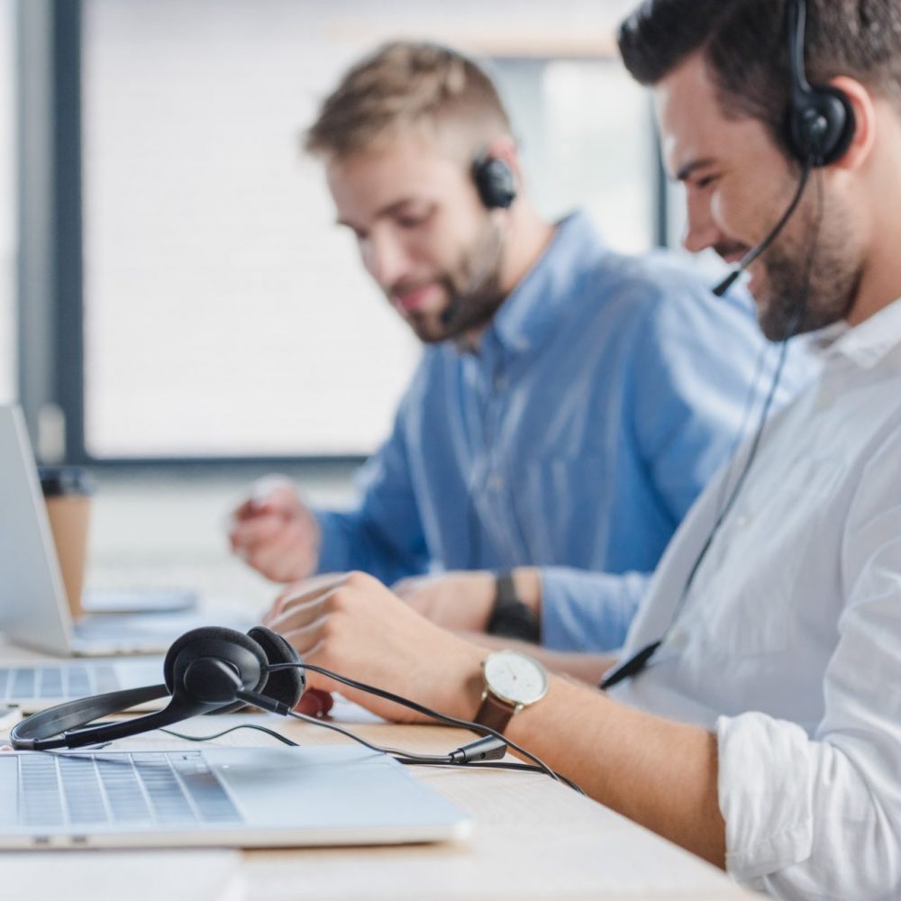 smiling young call center operators in headsets using laptops in office